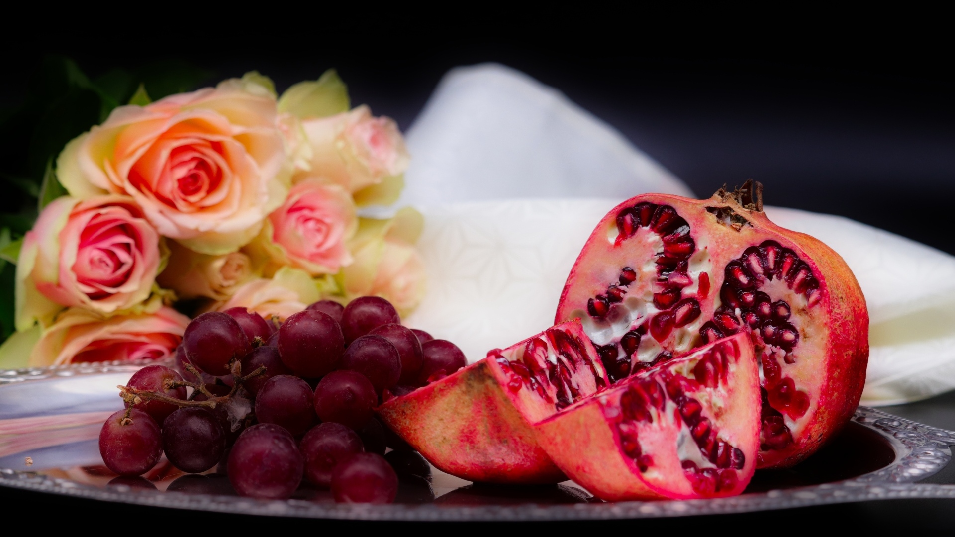 Гранат с виноградом на столе с букетом роз 