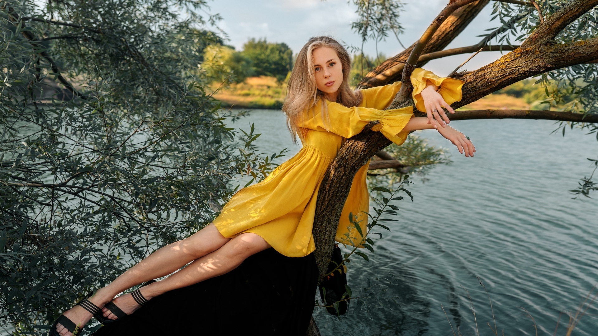 Красивая девушка в желтом платье лежит на дереве у воды
