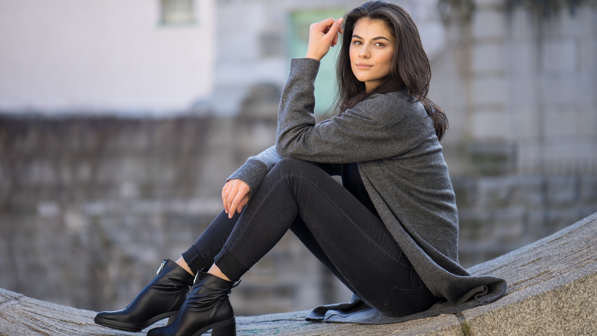 Милая девушка в сером наряде сидит на бетонной плите