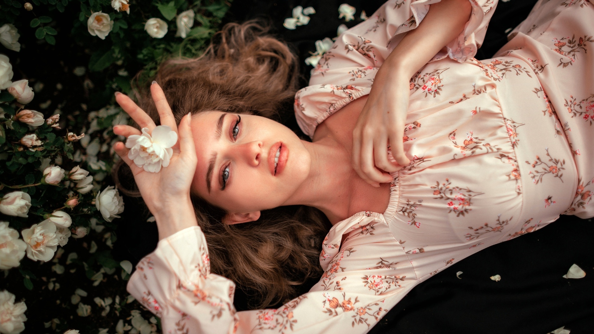 Девушка в розовом платье лежит на земле с цветами розы