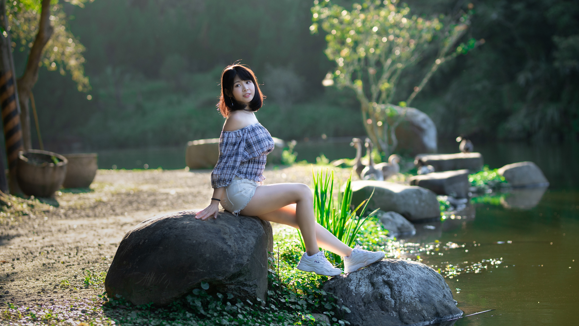 Девушка сидит на большом камне у пруда