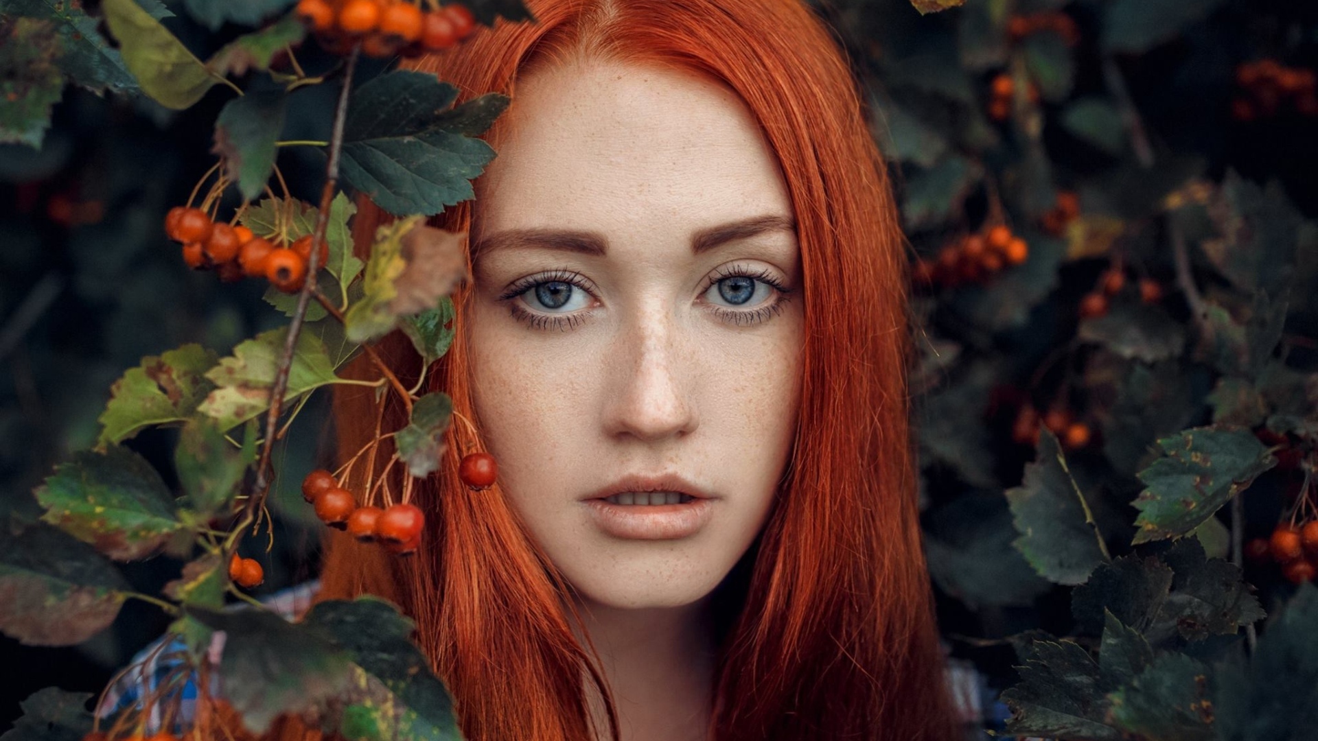 Рыжеволосая девушка стоит у куста с боярышником