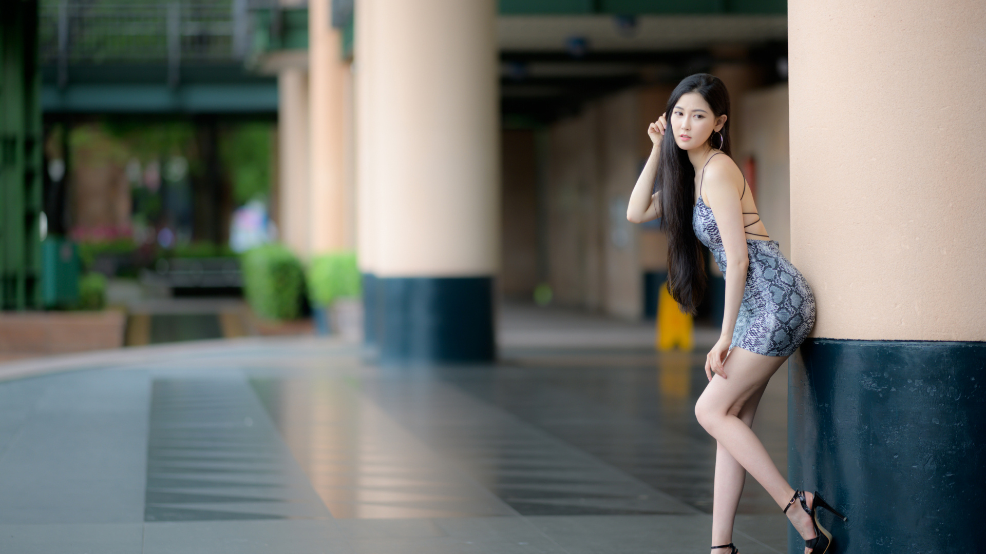 Стройная азиатка в коротком платье  стоит у колонны