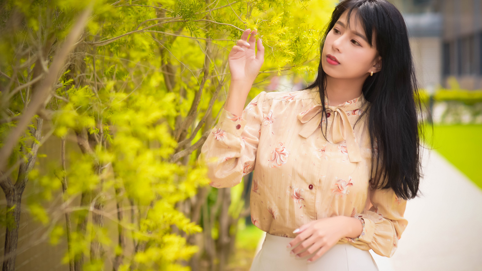 Молодая девушка азиатка стоит у дерева с зелеными листьями