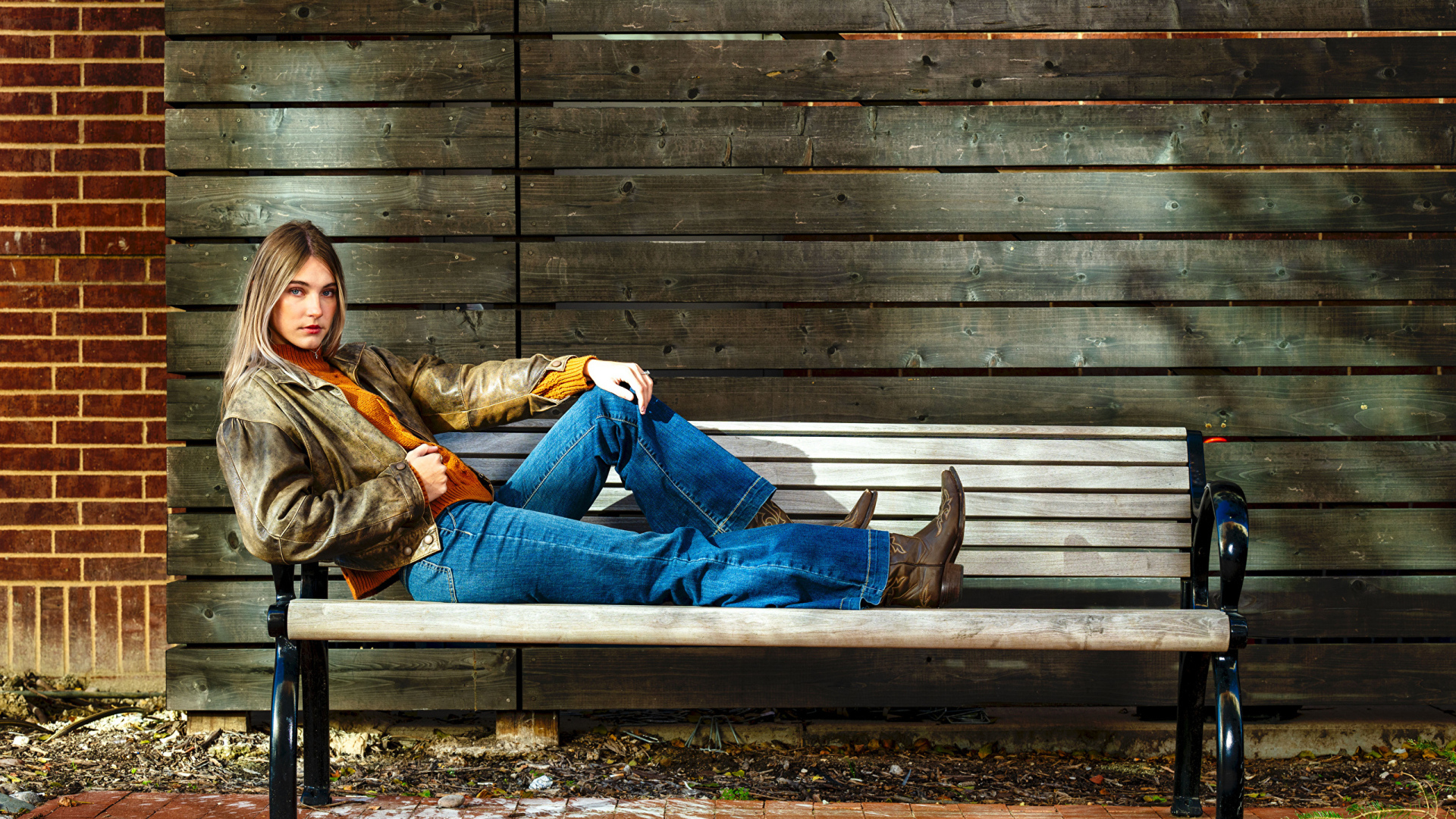 Молодая девушка в синих джинсах лежит на лавке