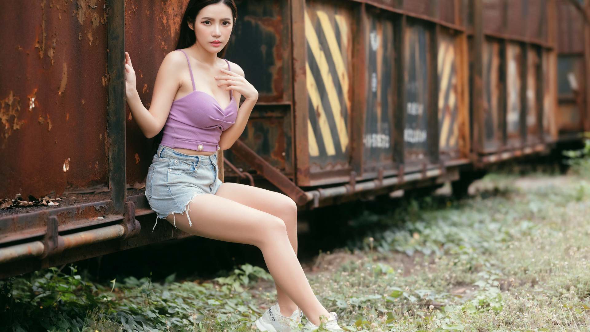 Девушка азиатка сидит у ржавого вагона