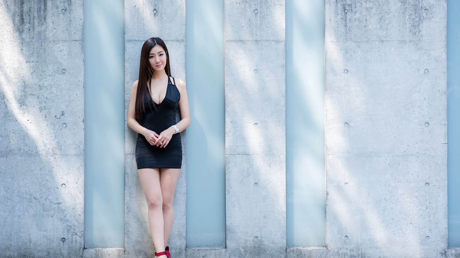 Красивая азиатка в коротком платье стоит у стены
