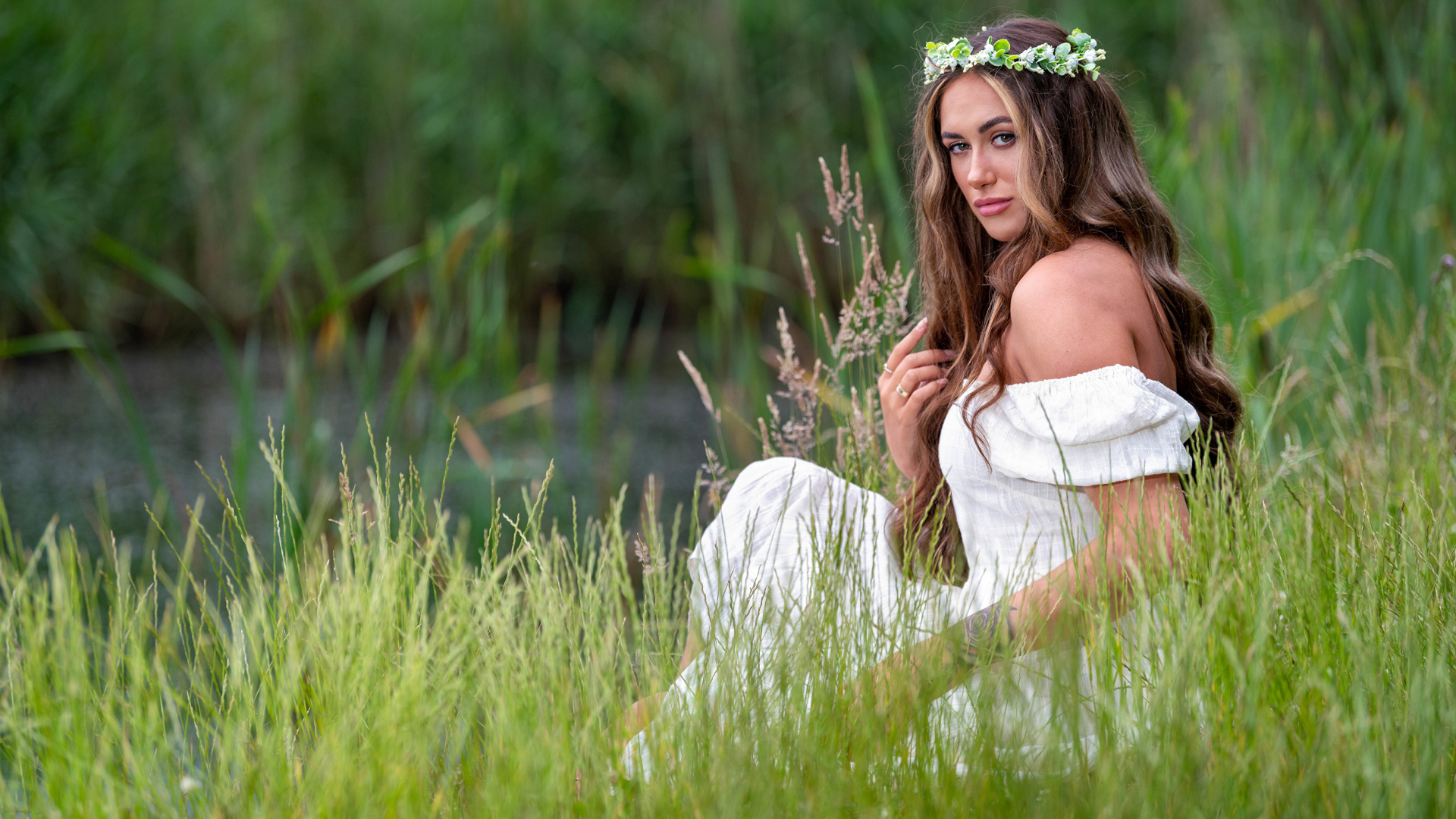 Красивая девушка в белом платье с венком на голове у пруда 