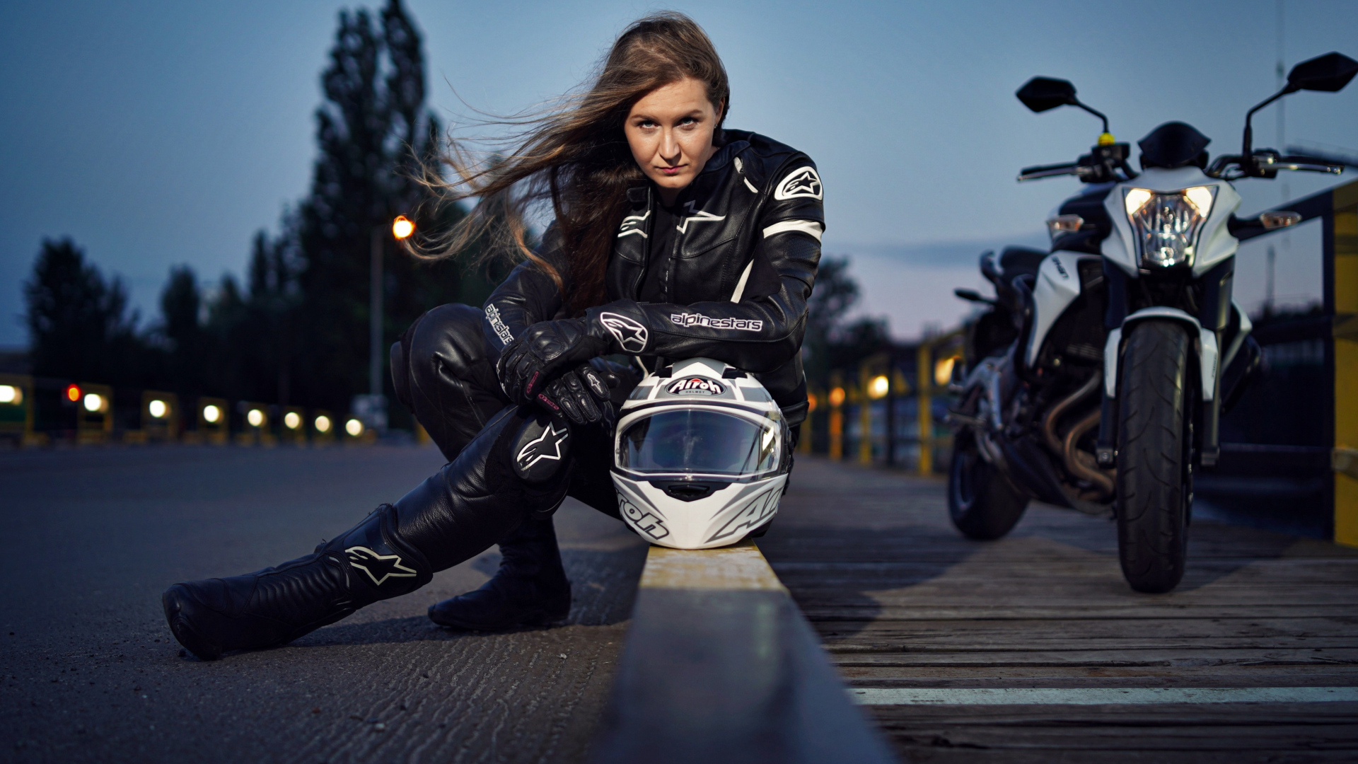 Красивая девушка с мотоциклом сидит на дороге