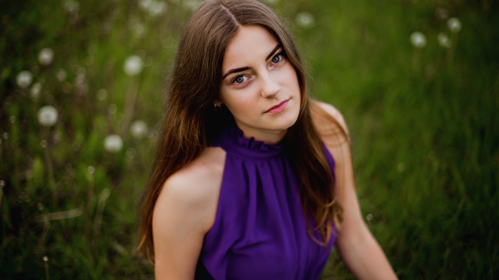 Милая девушка в фиолетовом платье сидит на траве