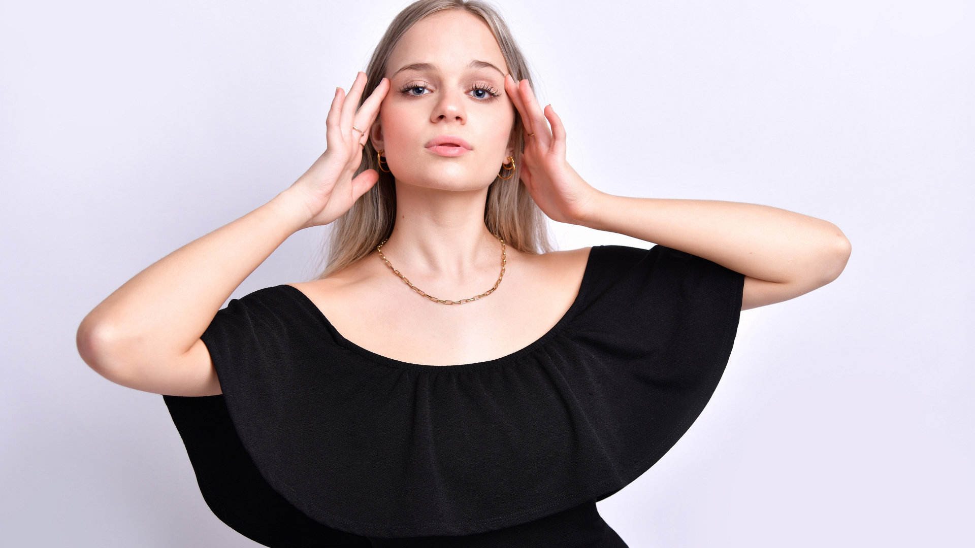 Девушка в черном платье с руками у головы на белом фоне