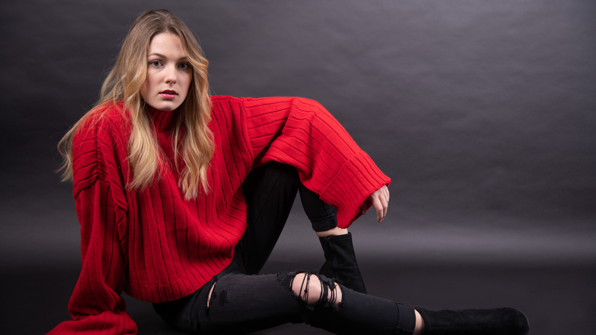 Девушка в красном свитере сидит на сером фоне