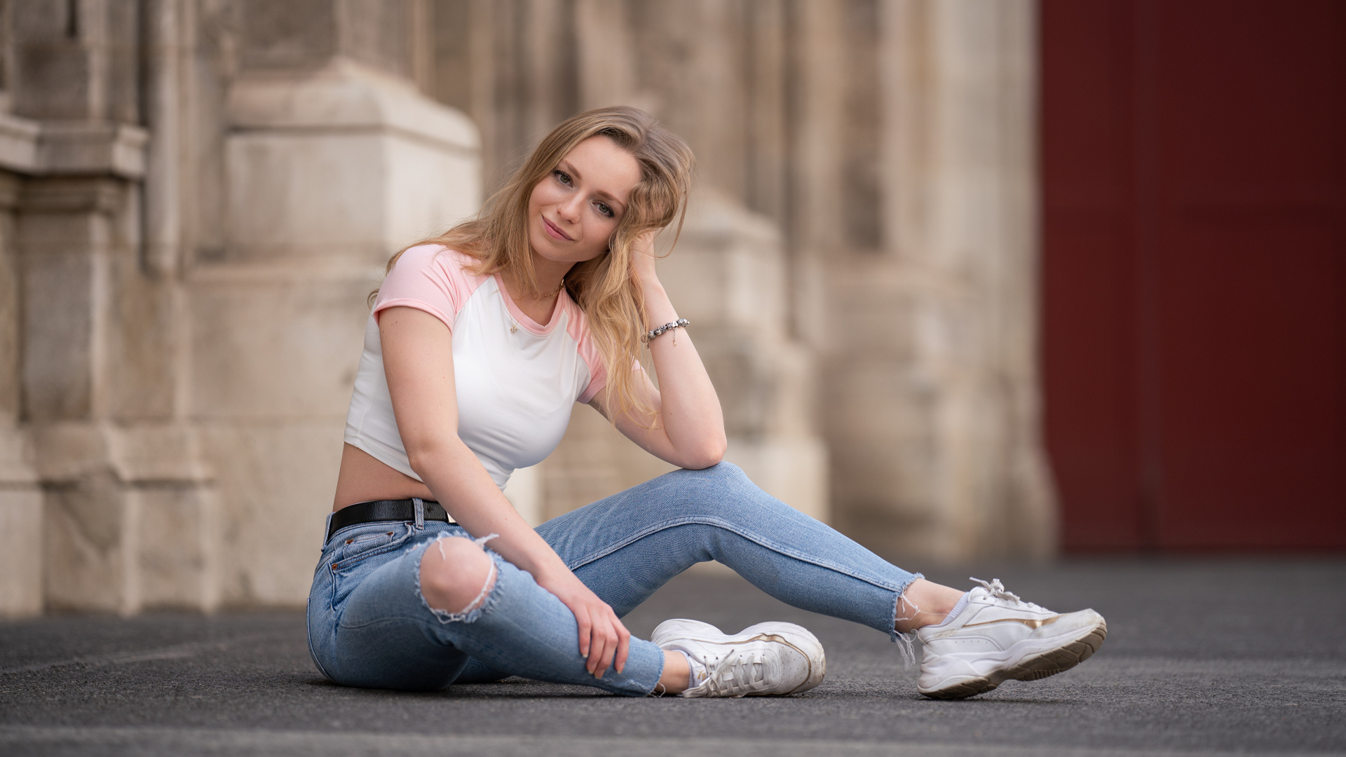 Девушка в рваных джинсах сидит на асфальте