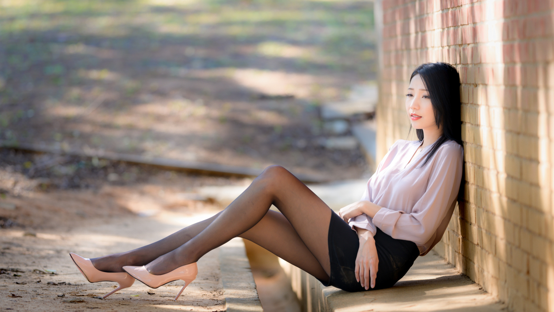 Грустная азиатка сиди у кирпичной стены