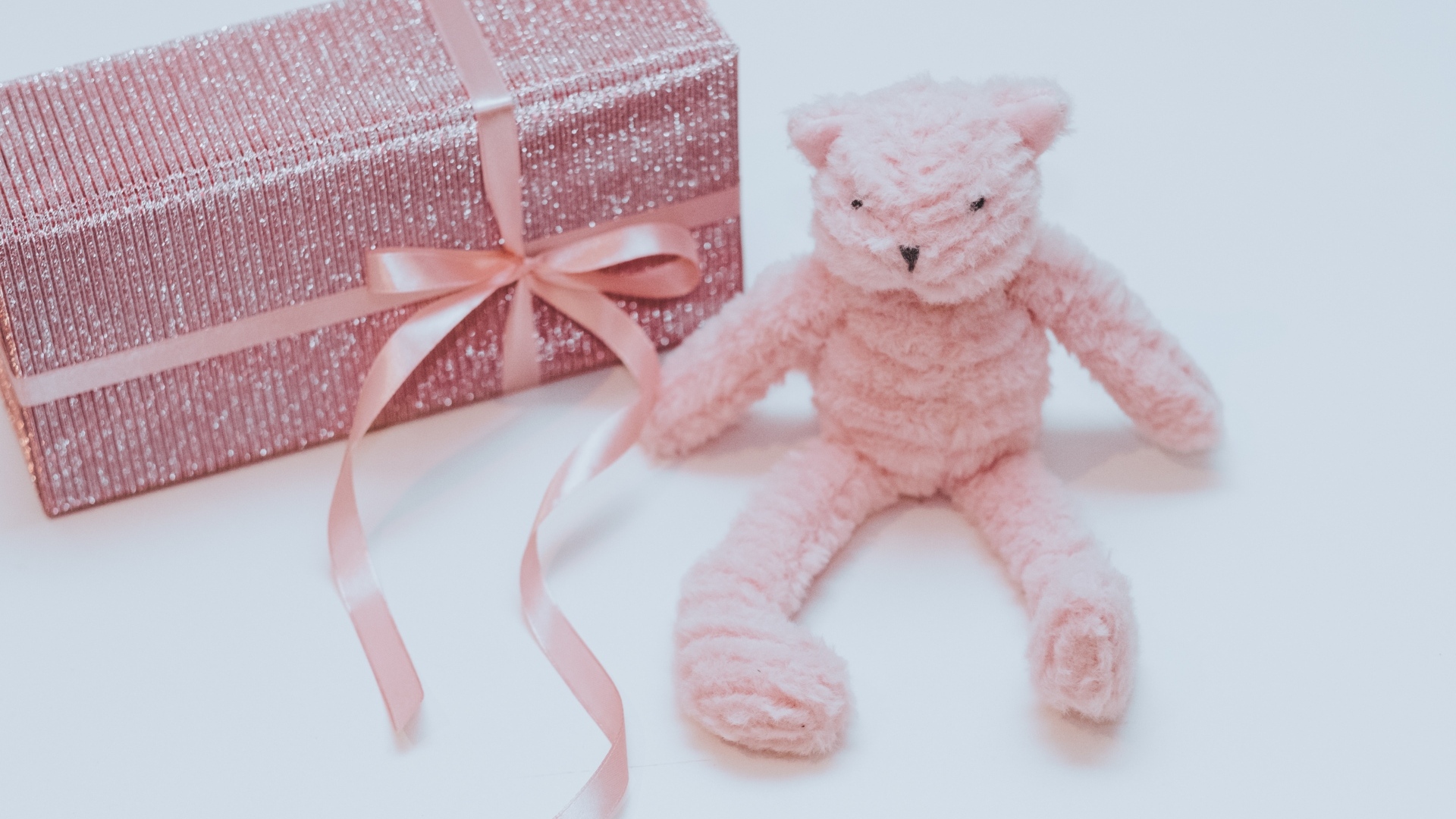 Подарок с розовой игрушкой на сером фоне