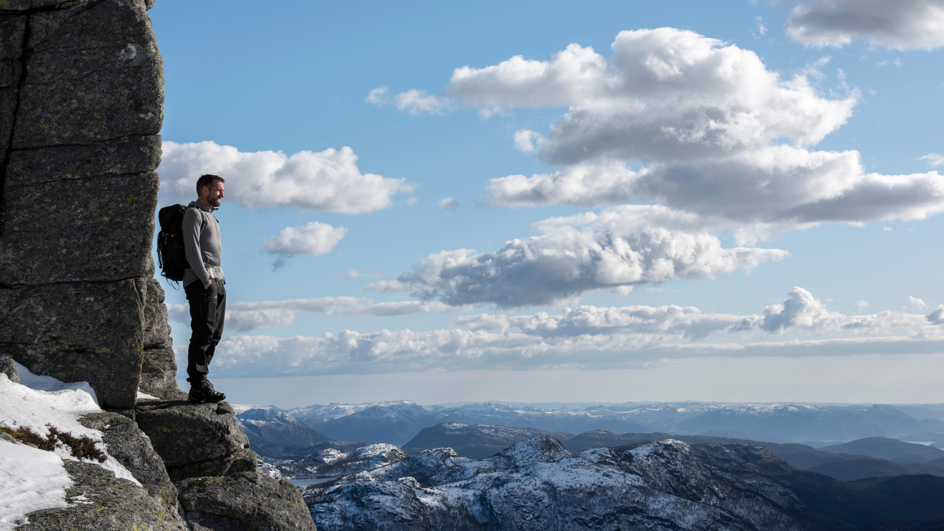 Мужчина стоит на краю скалы на фоне неба 