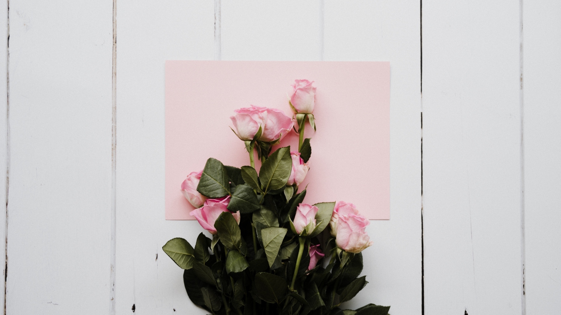 Букет роз с розовым листом бумаги на столе