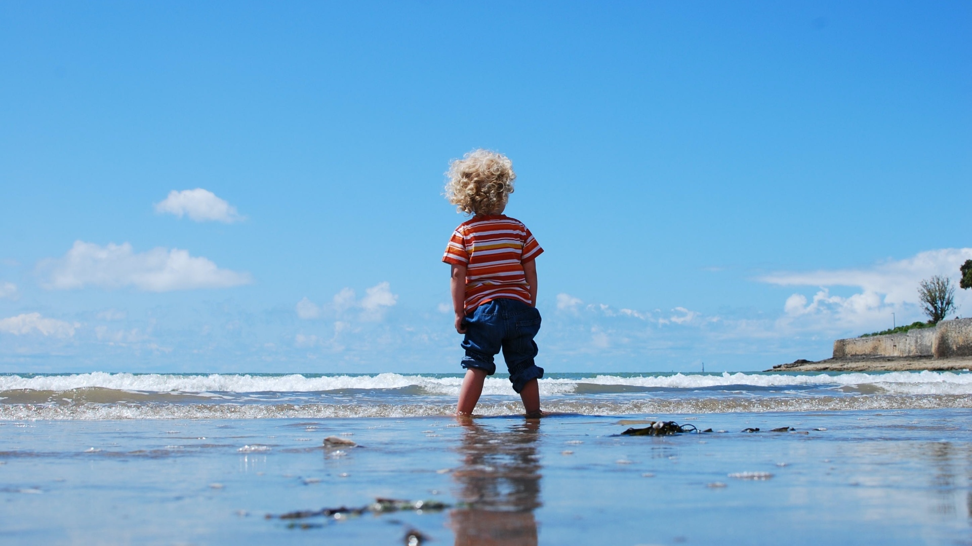 Маленький мальчик гуляет по мокрому песку у моря