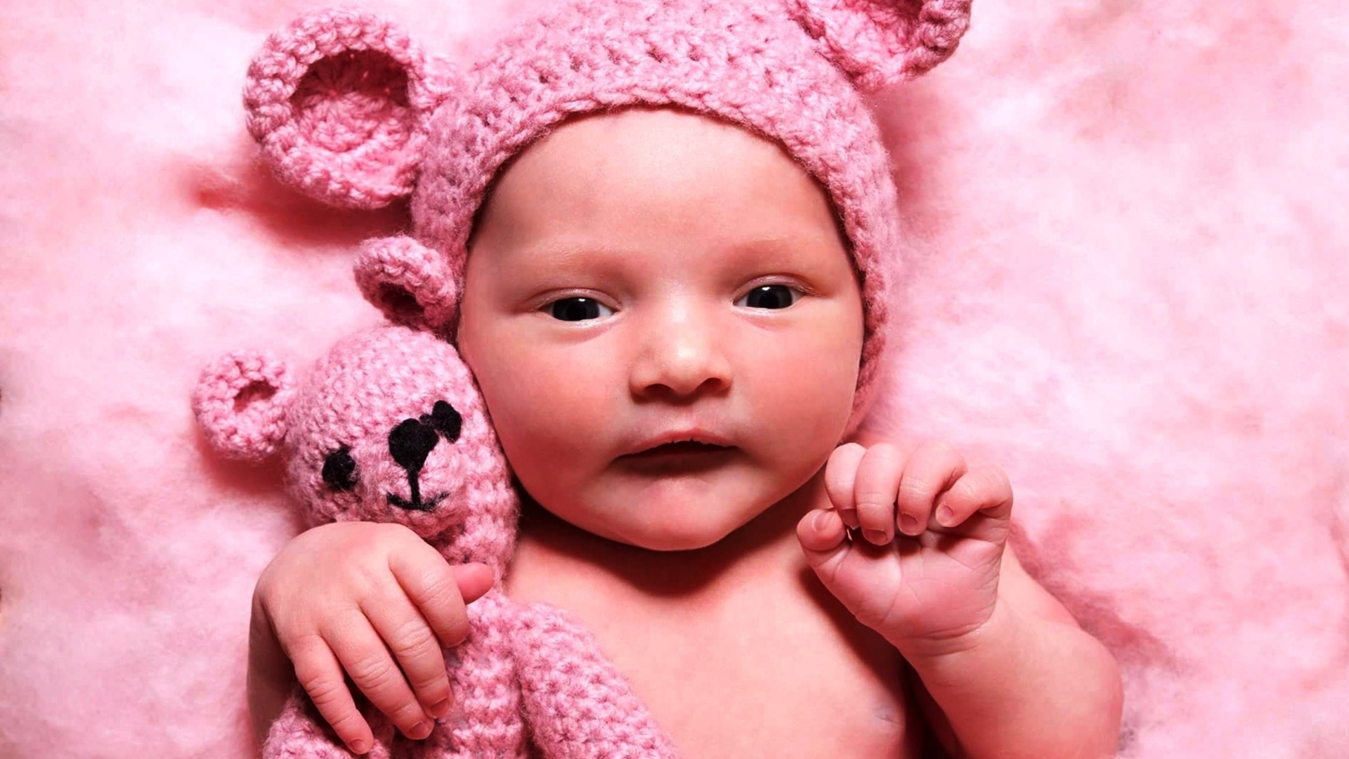 Грудной ребенок в розовой шапке с игрушкой в руке