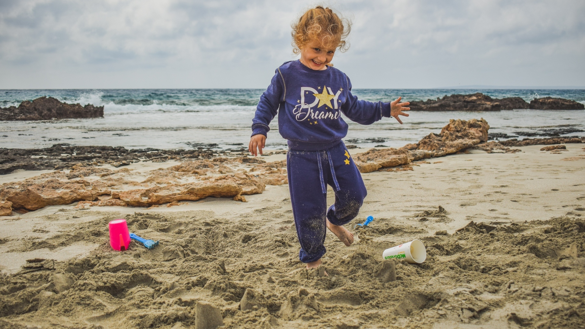 Веселая девочка играет на песке на пляже