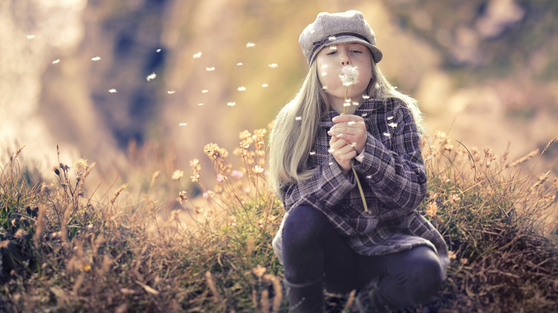 Девочка в кепке сдувает одуванчик