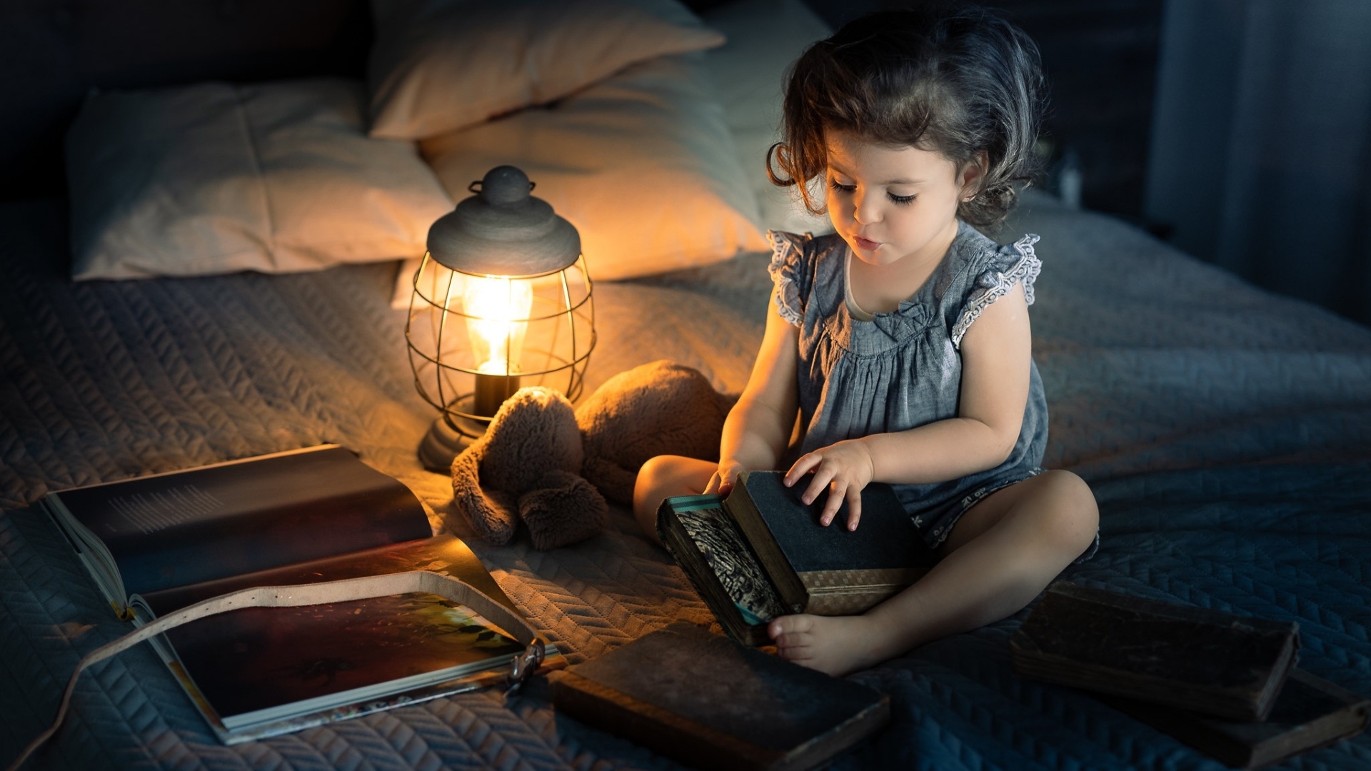 Маленькая девочка читает книги на кровати