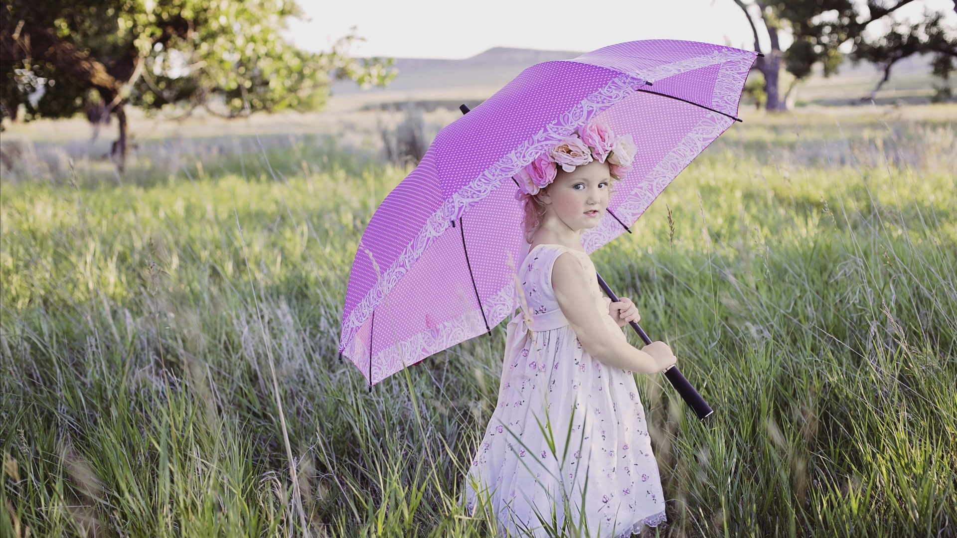 Маленькая девочка стоит в траве с зонтом