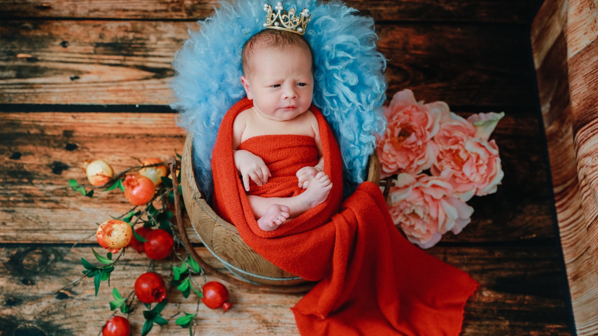 Новорожденный ребенок в красном покрывале с короной на голове 