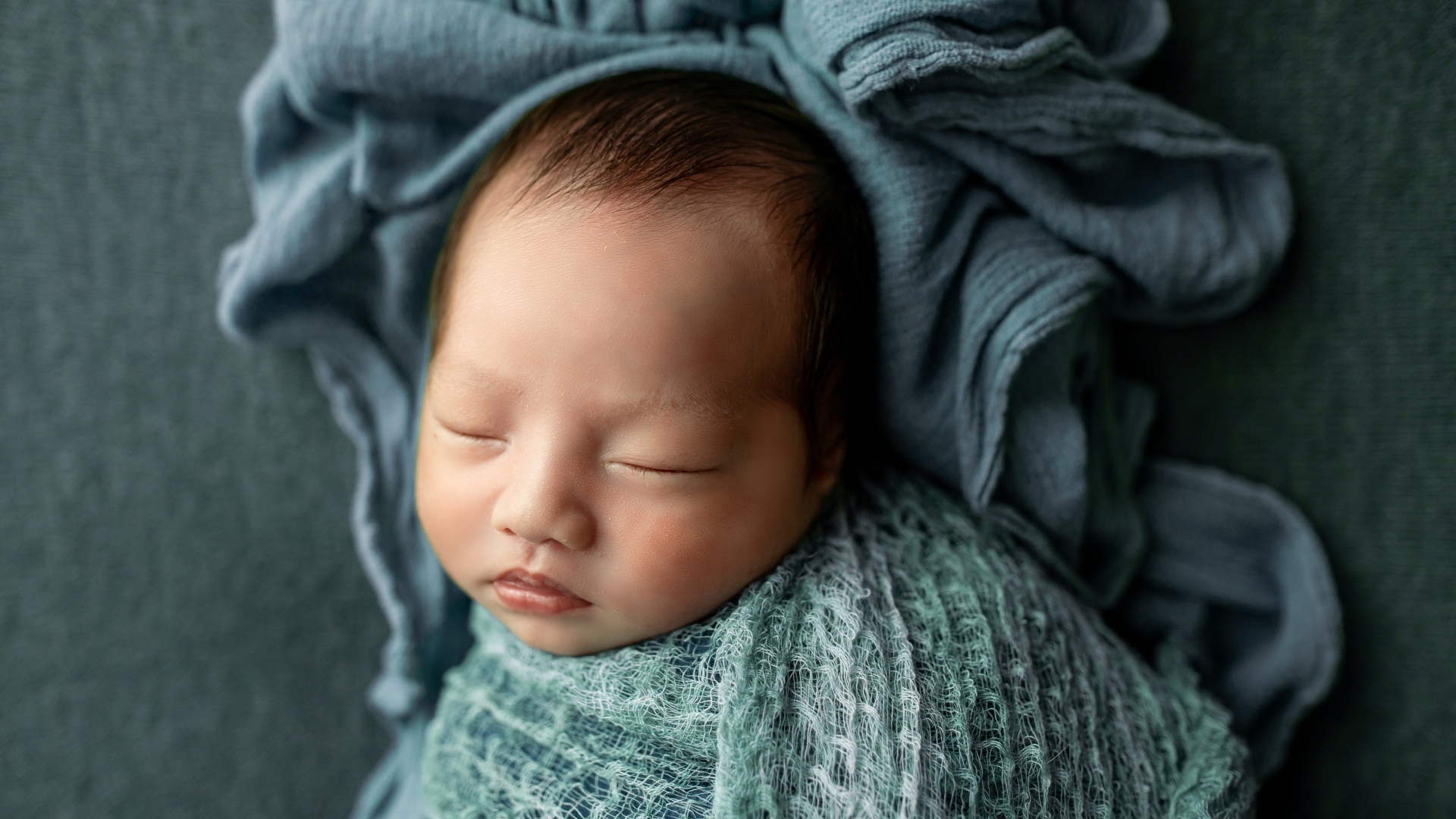Новорожденный ребенок завернут в серое покрывало 
