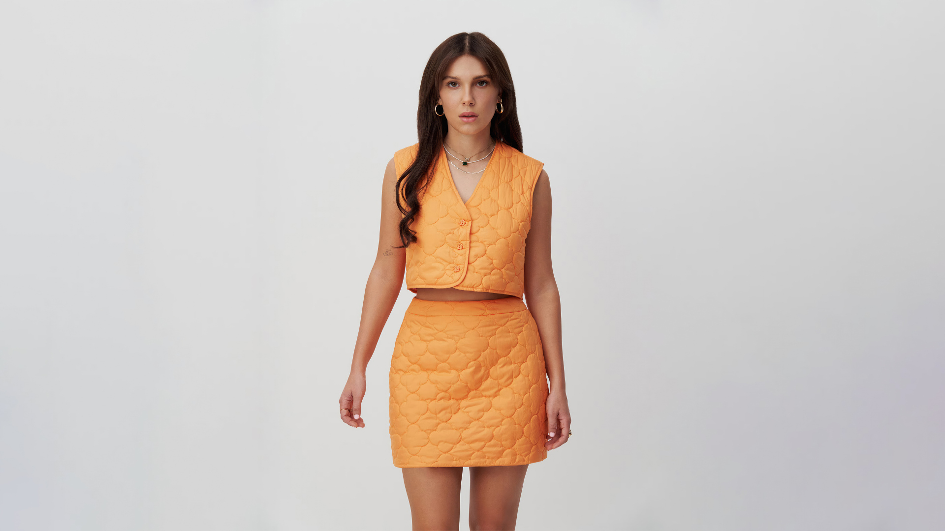 Девушка актриса Милли Бобби Браун в костюме на сером фоне