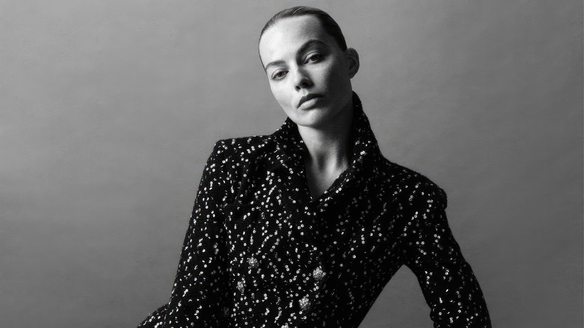 Грустная Марго Робби в блестящем пиджаке на сером фоне