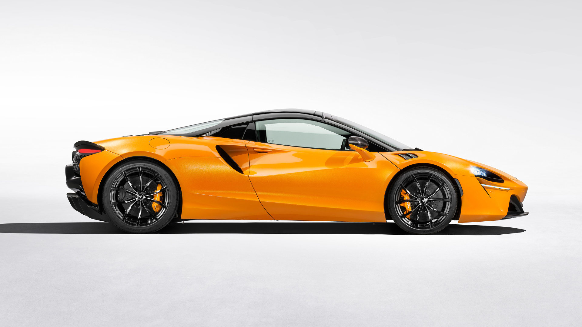 Вид сбоку на оранжевый автомобиль McLaren Artura Spider на белом фоне