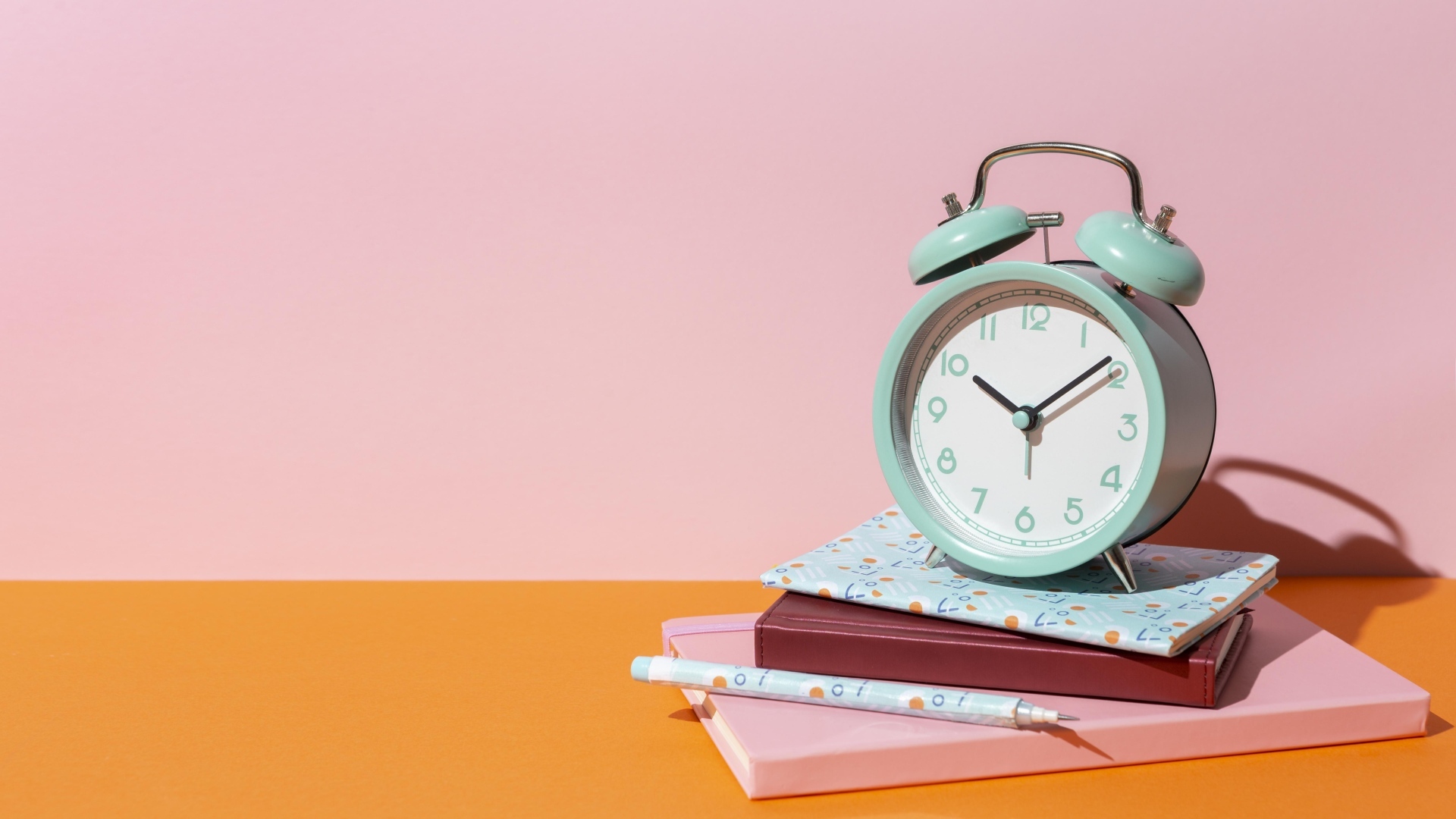 Будильник с книгами на розовом фоне