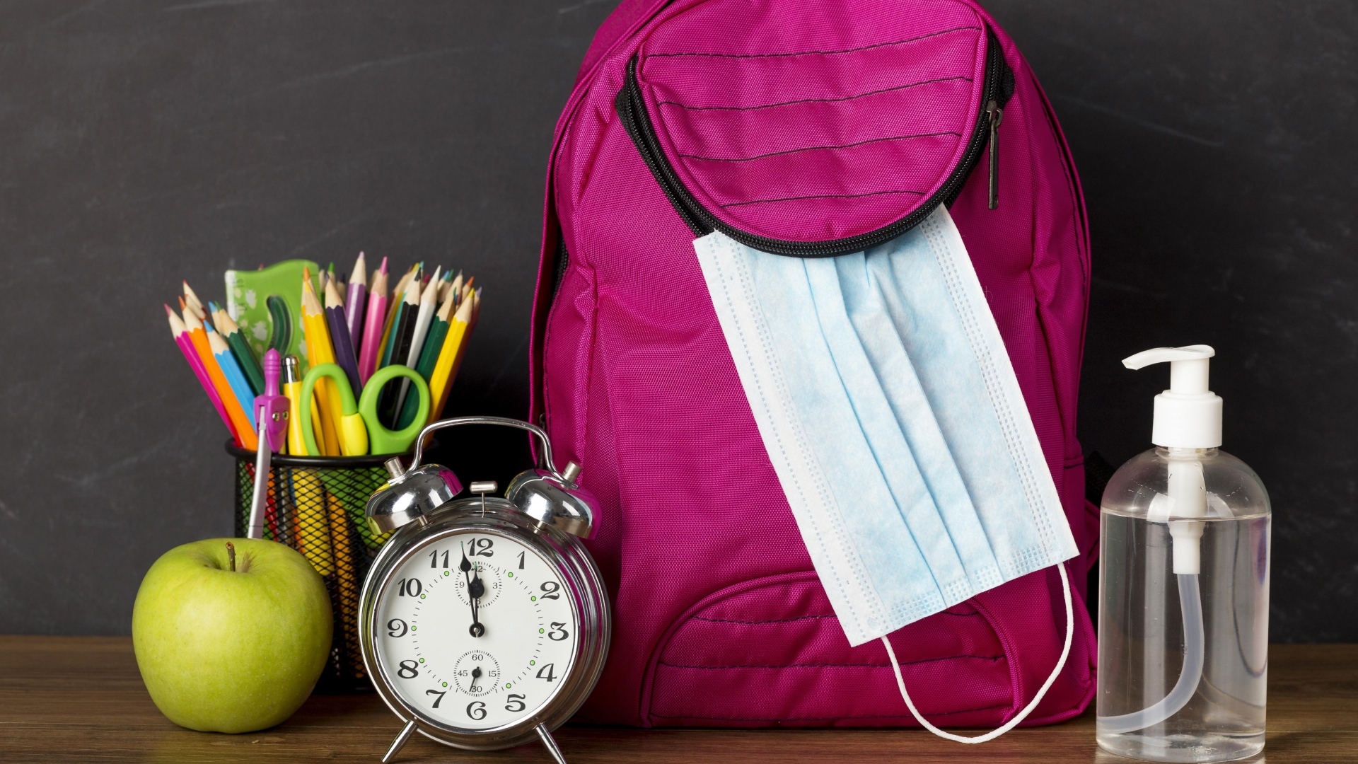Рюкзак на столе с будильником, ручками и яблоком