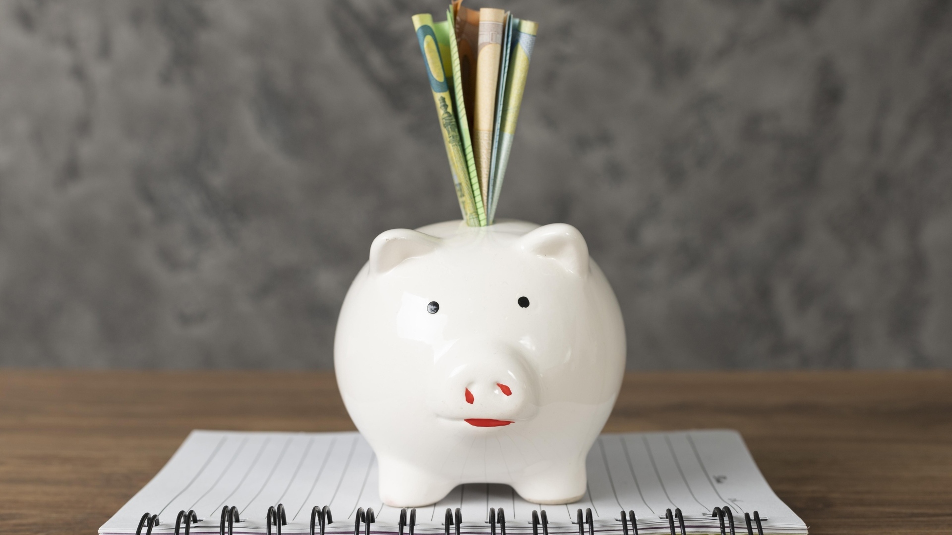 Свинья копилка с купюрами на столе с блокнотом