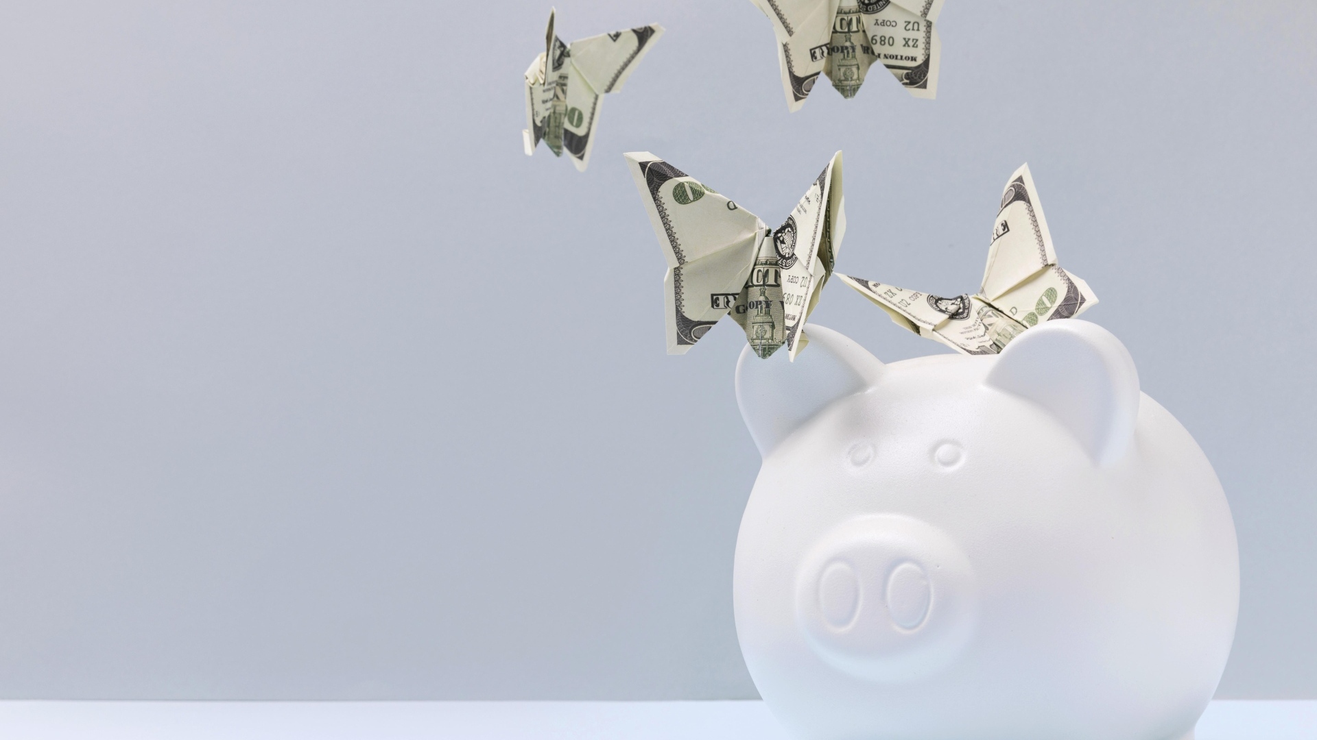 Свинья копилка с бабочками из купюр на сером фоне