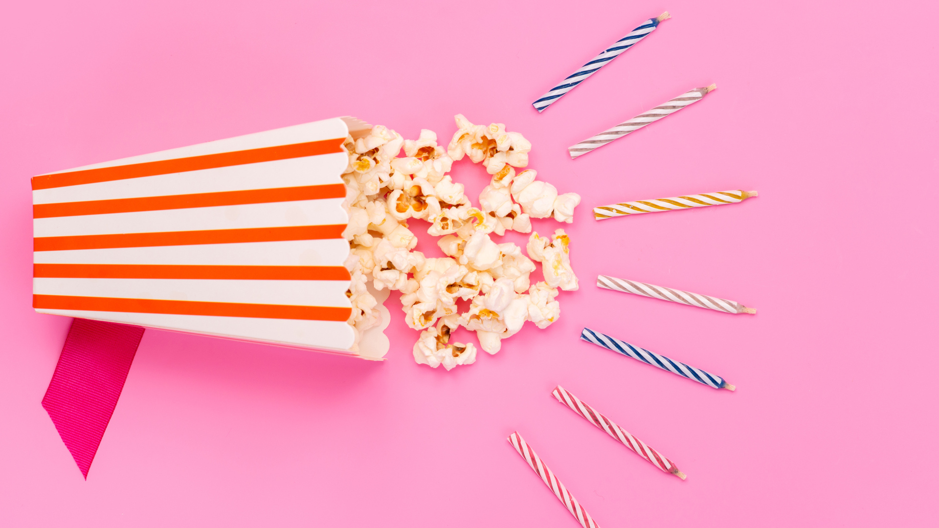 Коробка попкорна со свечами на розовом фоне