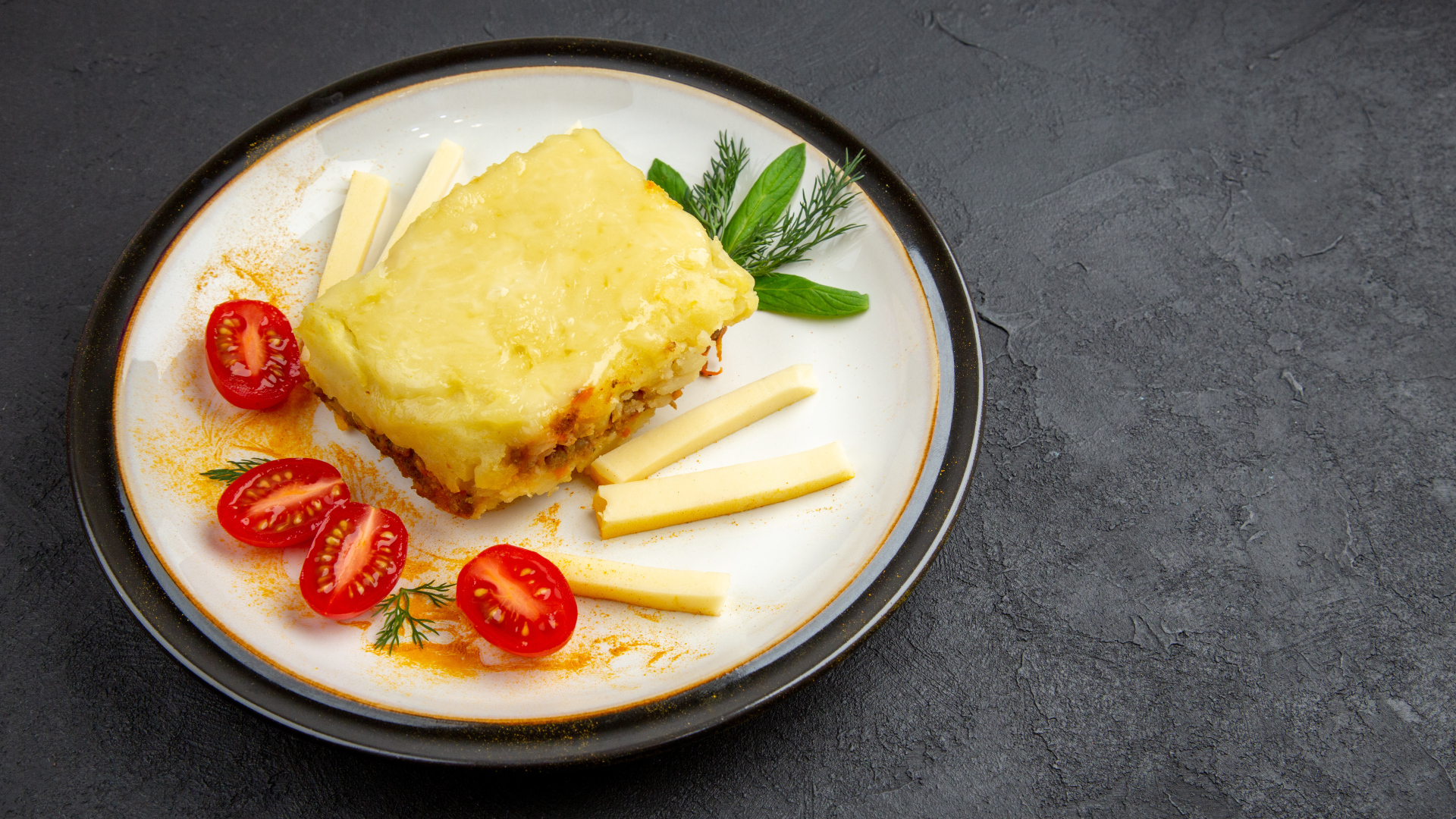 Кусок картофельной запеканки на тарелке с помидорами