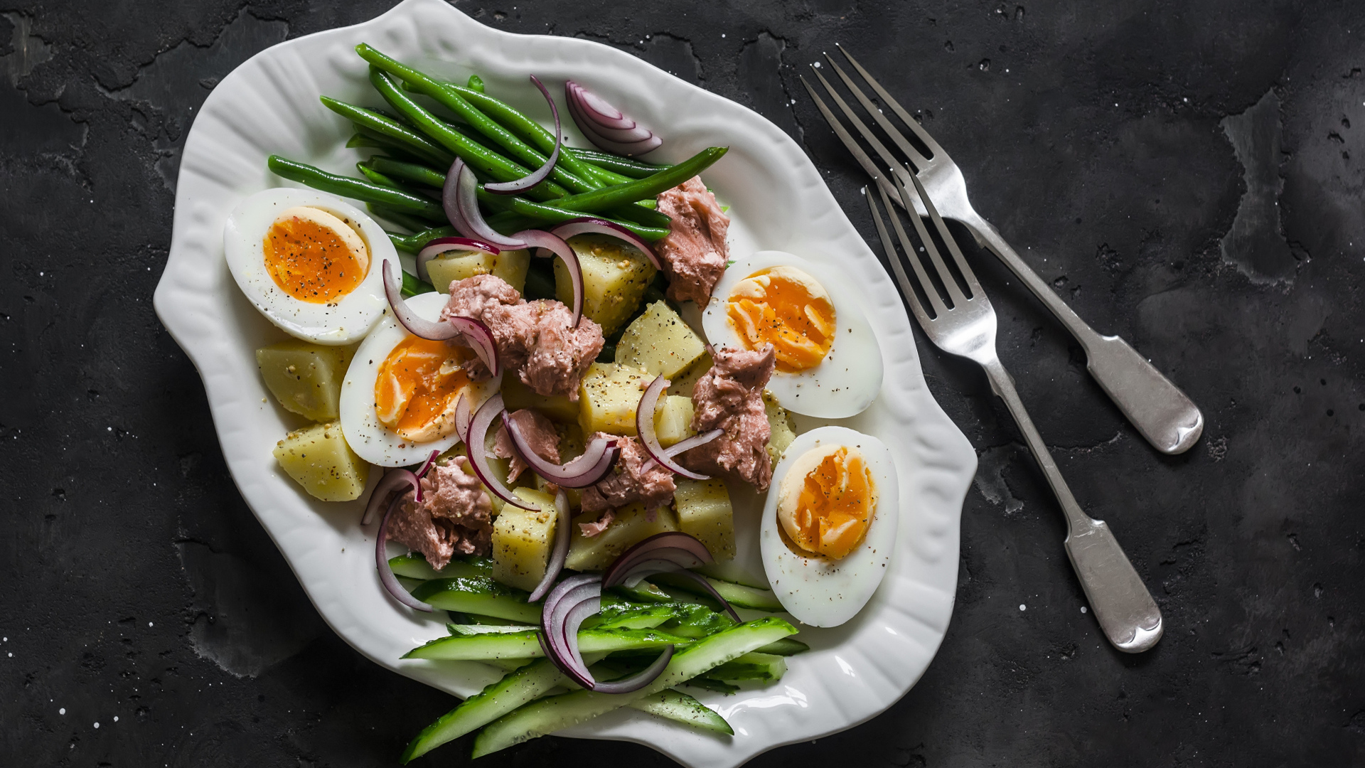 Картофель с мясом, яйцами, спаржей и огурцами на тарелке