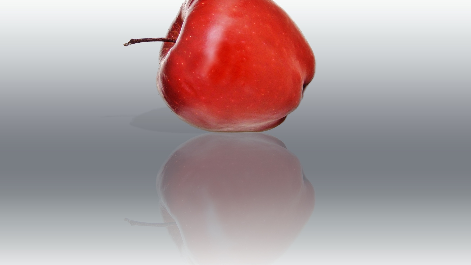 Красное яблоко отражается в серой поверхности