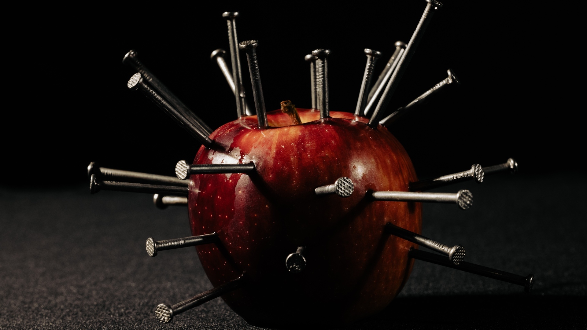 Красное яблоко утыканное гвоздями на темном фоне