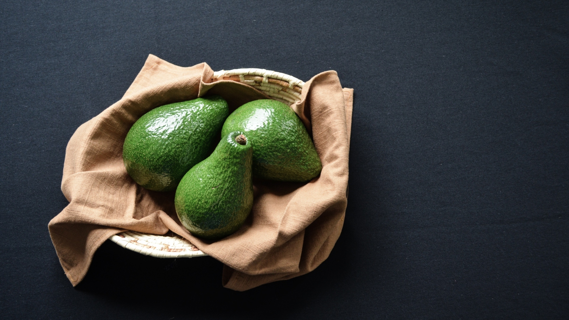 Три зеленых авокадо в корзинке на столе