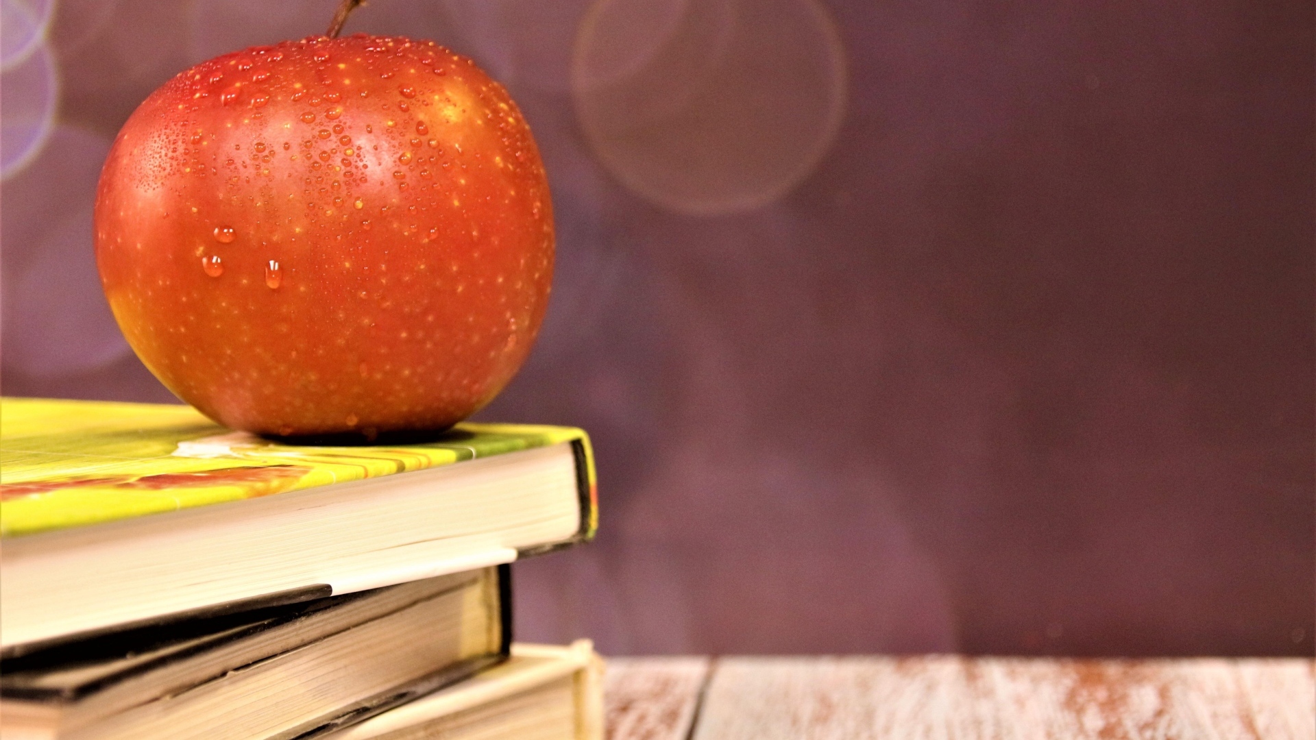 Мокрое яблоко на столе с книгами