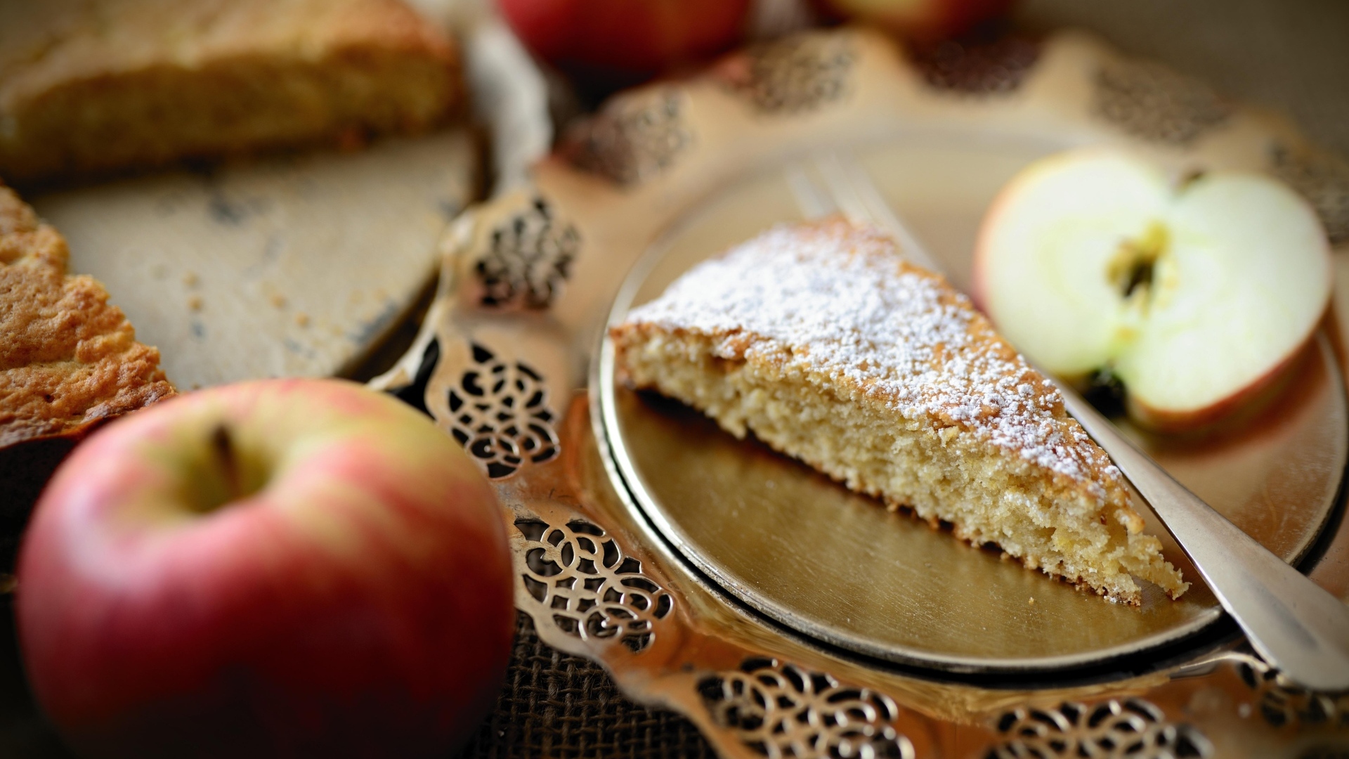 Кусок пирога с сахарной пудрой на столе с яблоками