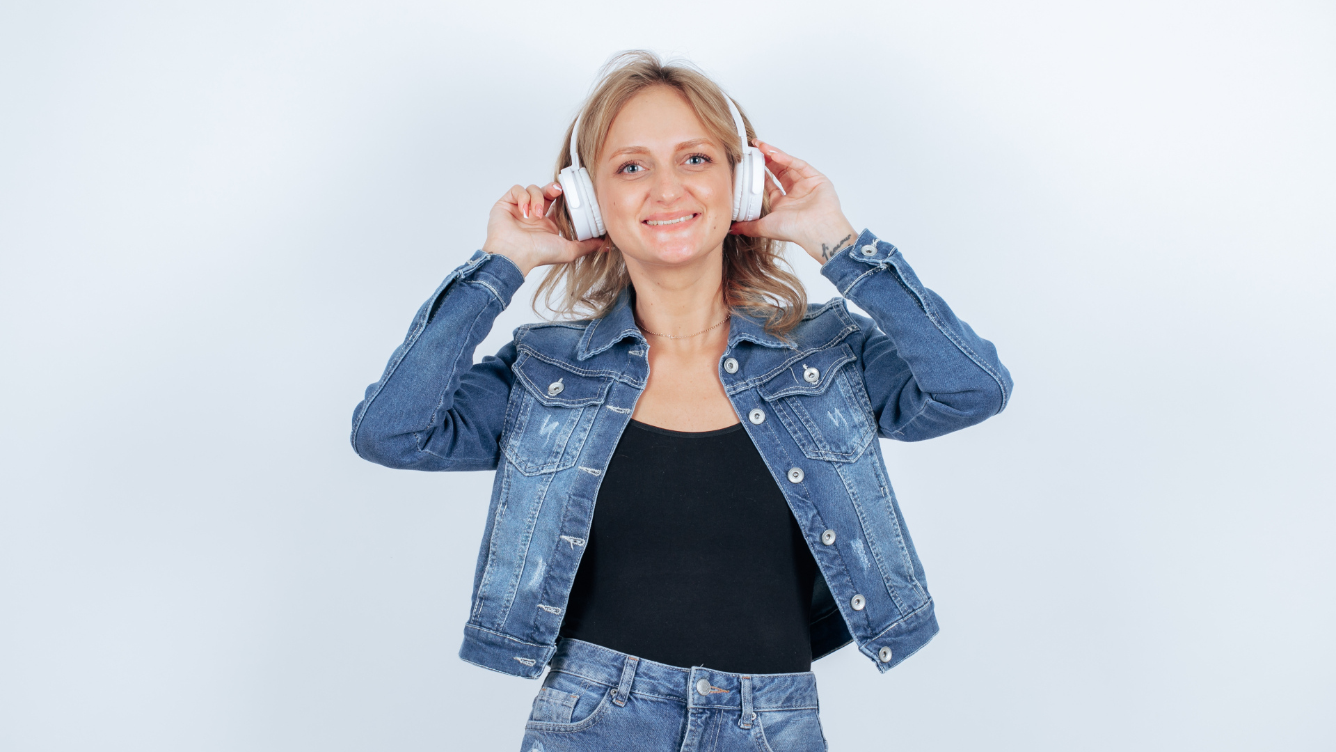 Девушка в джинсовом костюме с наушниками на голове на фоне стены