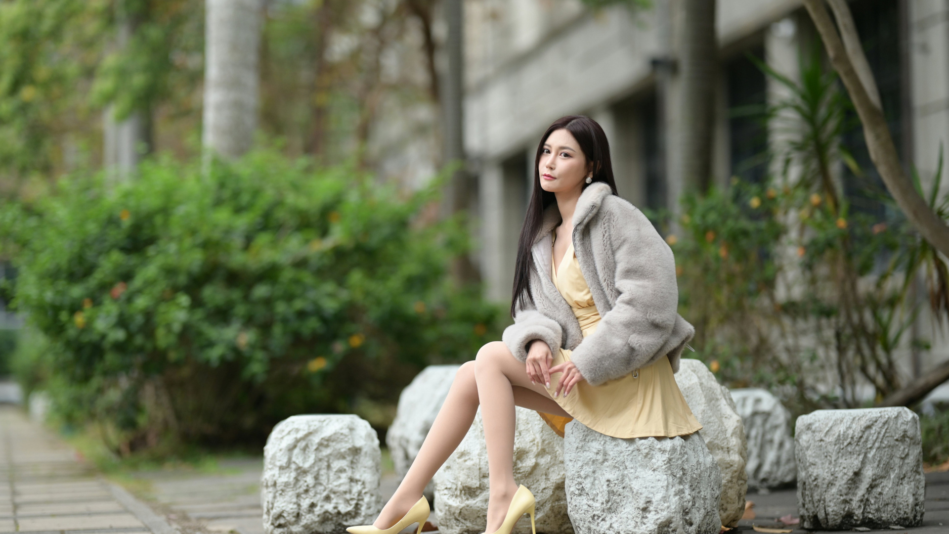 Азиатка в шубе сидит на квадратном камне