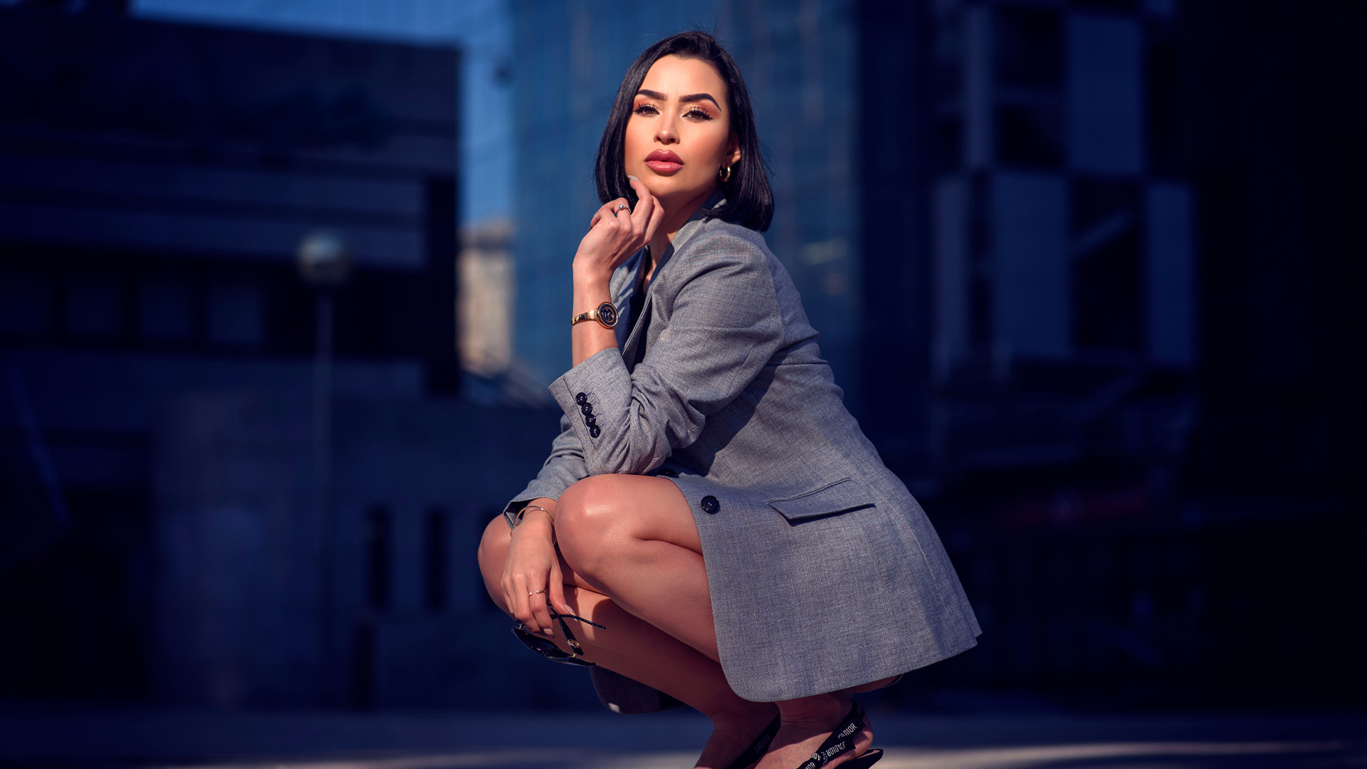 Красивая брюнетка в сером пиджаке сидит на корточках