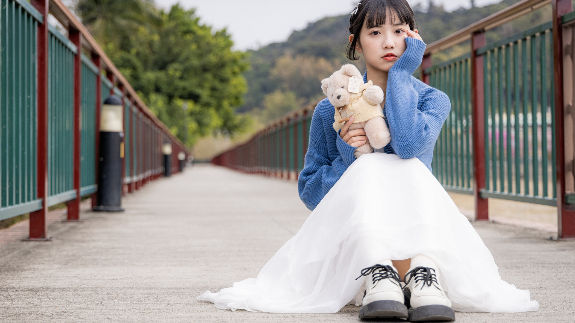 Милая азиатка с игрушечным медвежонком сидит на мосту