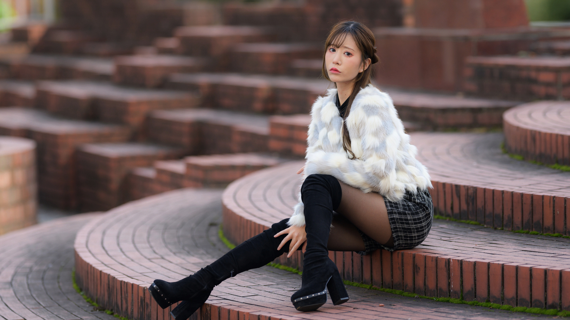 Грустная азиатка в шубе сидит на ступеньках