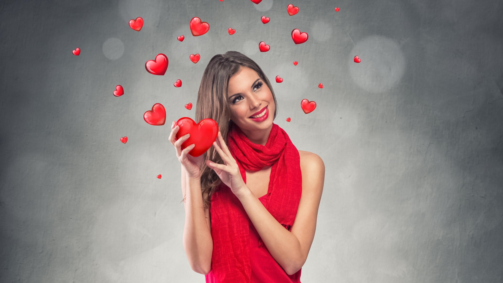 Улыбающаяся девушка в красном платье с сердечками на сером фоне